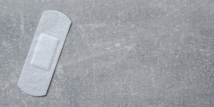 Adhesive white bandage on the stone background, piece of plaster sticking out.