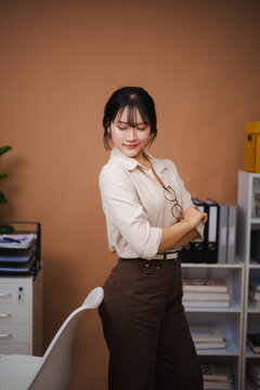 Confident young woman standing in modern office with arms crossed and smiling wearing casual professional outfit