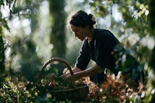 Older woman crouching beside a basket on the forest floor. Foraging, slow living and connection with nature