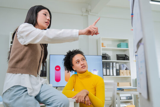 A busy modern office captured through blurred foreground papers: a man reviews documents while two diverse colleagues chat nearby, capturing authentic depth, focus and genuine multitasking workplace e