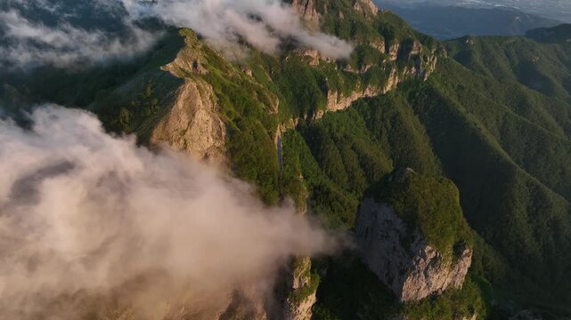 Aerial view of Foce del Pallone mountain range with rocky peaks and lush green slopes partially covered by clouds in Stazzema, Toscana, Italy.
