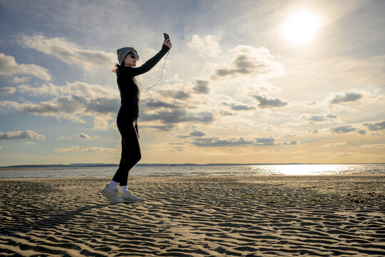 Woman Runner Taking a Selfie on Beach at Sunset with Phone