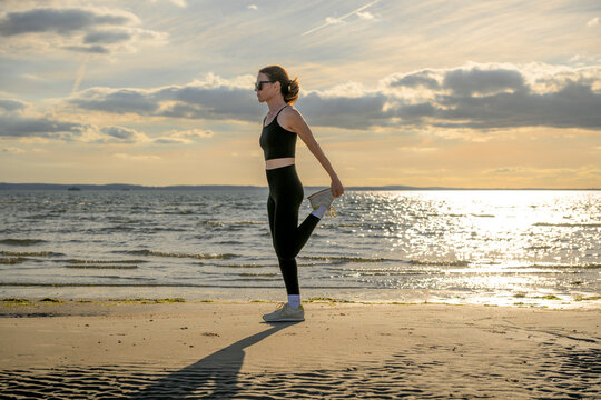 Woman Preparing for a run on a Beach at Sunset, Leg Stretch