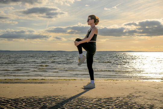 Woman Runner doing a Leg Stretch Exercise on Beach at Sunset