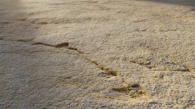 Beige foamy liquid slowly spreads across a rough textured ground surface