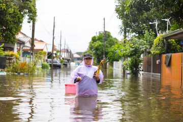 Fototapeta premium obese woman wearing Raincoat and walking through flood waters to go buy food, lifestyle of Thai people in massive flooding, Severe weather