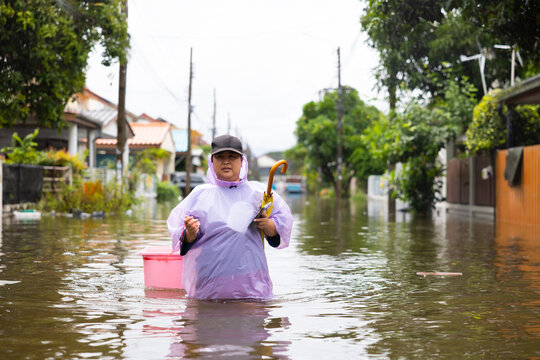 obese woman wearing Raincoat and walking through flood waters to go buy food, lifestyle of Thai people in massive flooding, Severe weather