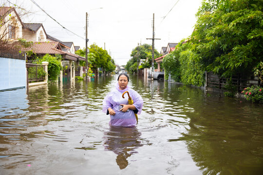 obese woman wearing Raincoat and walking through flood waters to go buy food, lifestyle of Thai people in massive flooding, Severe weather