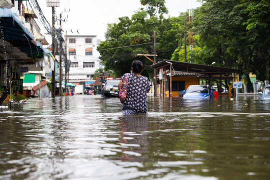 Senior woman walking through flood waters to go buy food, Evacuate to shelter. lifestyle of Thai people in massive flooding, Severe weather