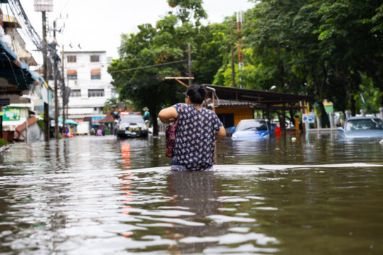 Senior woman walking through flood waters to go buy food, Evacuate to shelter. lifestyle of Thai people in massive flooding, Severe weather