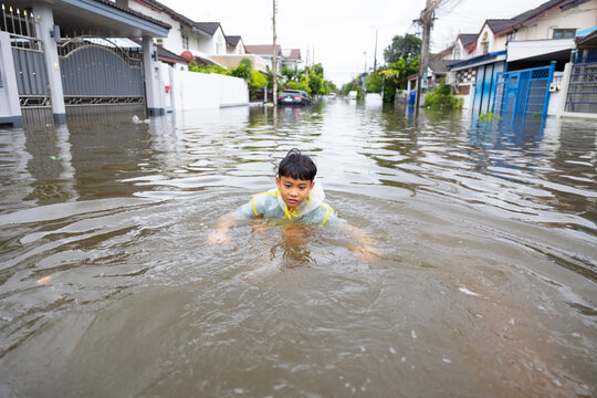 Standing in flood. Asian boy wearing Raincoat walking through floodwaters, lifestyle of Thai people in massive flooding, Severe weather