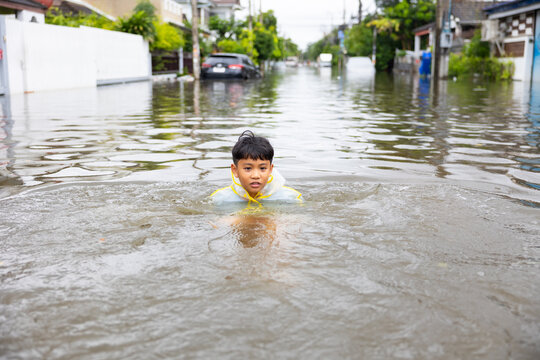 Standing in flood. Asian boy wearing Raincoat walking through floodwaters, lifestyle of Thai people in massive flooding, Severe weather