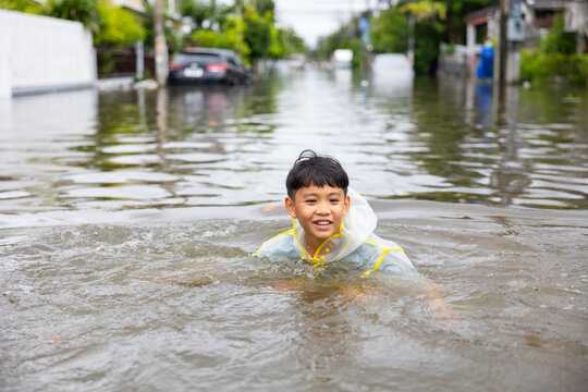 Standing in flood. Asian boy wearing Raincoat walking through floodwaters, lifestyle of Thai people in massive flooding, Severe weather
