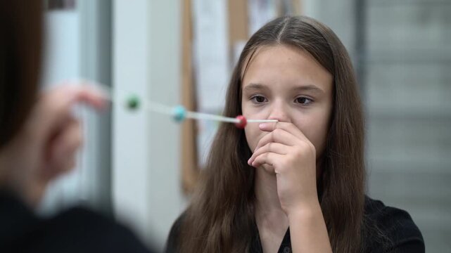 Mother and daughter do eye gymnastics with a beaded string to train focus and vision at home.