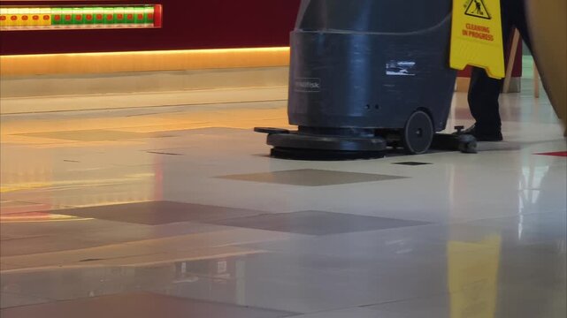 Janitor operating a commercial floor scrubber machine in a modern public building
