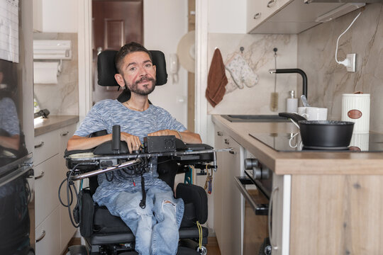 A man using a wheelchair is in a modern home kitchen. He appears happy and comfortable in his accessible living space.