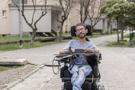 Portrait of a man with disability sits in a wheelchair on a pathway at urban area.