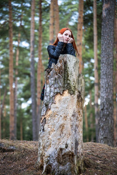 Red-haired woman poses beside weathered tree stump
