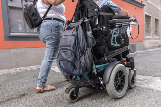 A man in a wheelchair receives support from a woman on an urban street. They navigate through the city together.