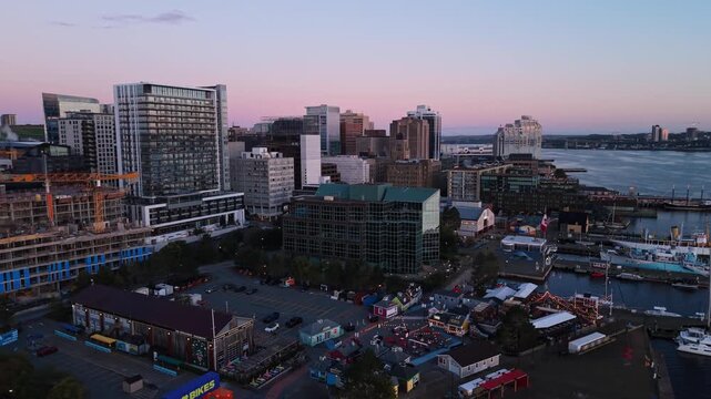 Aerial cinematic panorama of downtown Halifax at sunrise, showing intense red sunlight striking the skyscrapers while passenger ferries and large vessels travel across the harbour beside the city cent