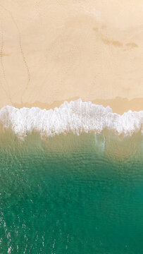 Aerial view directly above soft white waves lapping a golden sandy beach