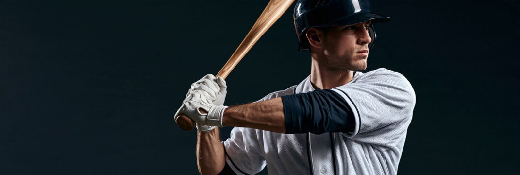Baseball player grips bat, poised for swing. Focused eyes, steady stance, intense concentration. Dark backdrop highlights athletic form and gear. Ideal for sports, fitness