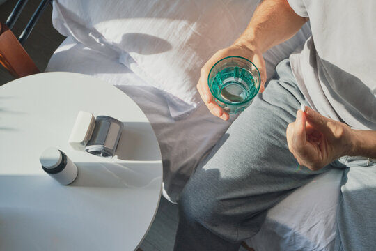 Man holds pill and glass of water, about to take high blood pressure medication at home