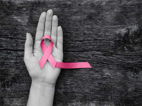 Reast cancer awareness month a pink awareness ribbon held in an open palm against a rustic dark wooden background, symbolizing support and hope for breast cancer awareness and health advocacy