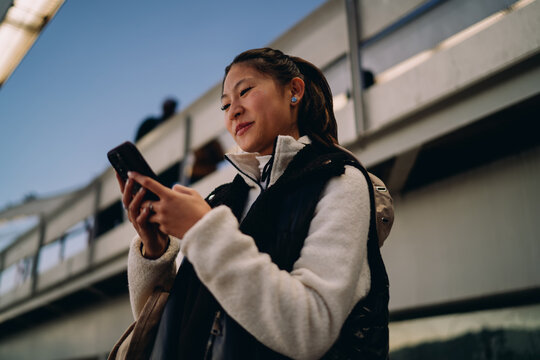 Asian woman looking at smartphone screen, digital nomad lifestyle, mobile application, technology connection, authentic representation, inclusion, real people, urban setting, communication, online