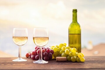 Obraz premium Wine glasses and bottle on wooden table. Fresh red and green grapes with cork. Sunset vineyard background