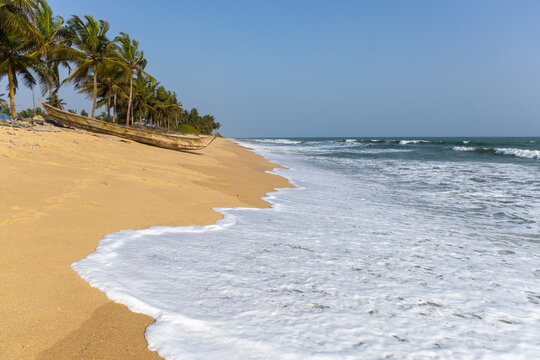 Wooden fishing boat on empty palm-lined beach, Elmina, Ghana