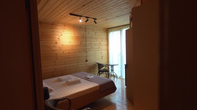 Comfortable and clean hotel room interior with a freshly made double bed, towels, and slippers, featuring rustic wooden walls and floors for a cozy and welcoming vacation accommodation