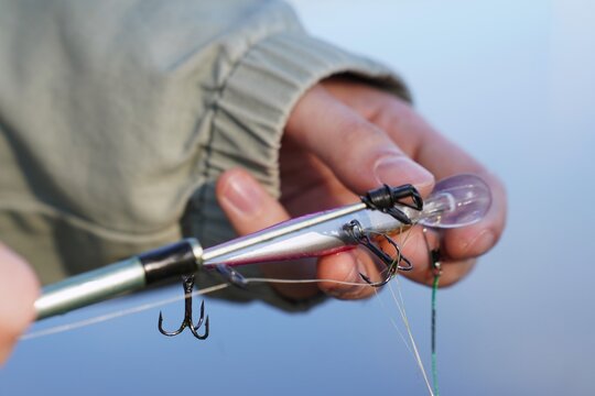 Fisherman hands untangling fishing line from wobbler lure with treble hooks on river in autumn. Tangled line problem during fishing. Closeup of tackle repair and angling equipment detail.