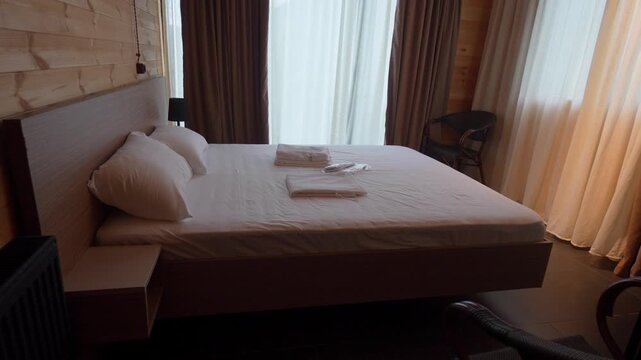 Comfortable and clean hotel room interior with a freshly made double bed, towels, and slippers, featuring rustic wooden walls and floors for a cozy and welcoming vacation accommodation