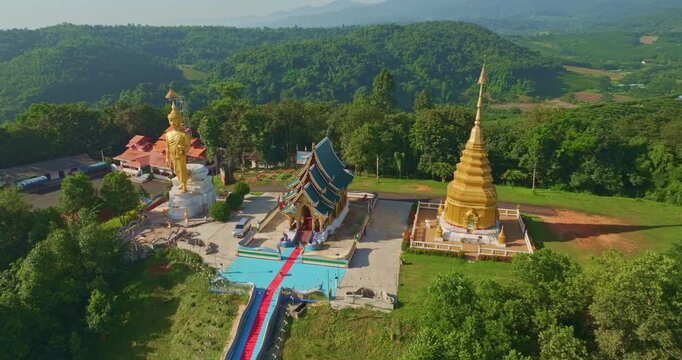 A majestic golden Buddha statue surrounded by lush green trees, set against a stunning backdrop of rolling mountains and a clear blue sky. This serene landscape captures the harmony of spirituality