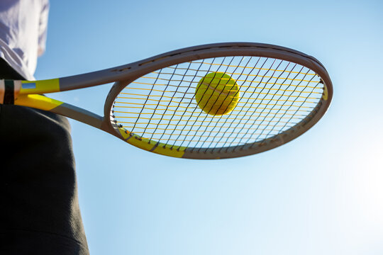 Tennis racket holding a ball under a clear blue sky in bright daylight