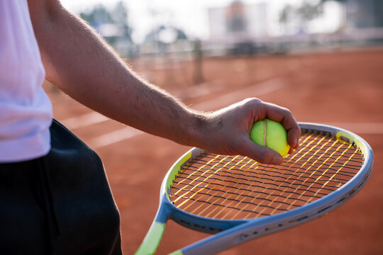 Close up of a tennis player placing a ball on racket strings on a clay court