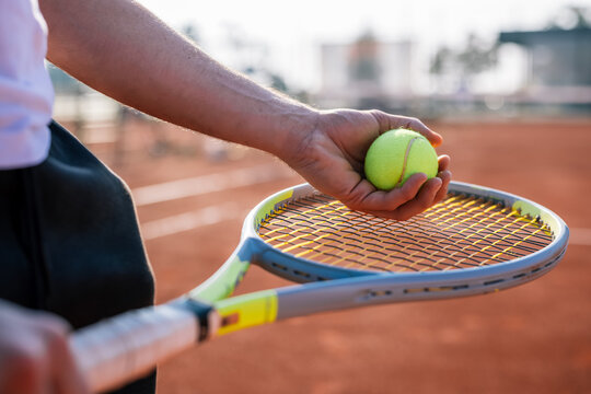 Close up view of a hand holding a tennis ball over racket head before serving