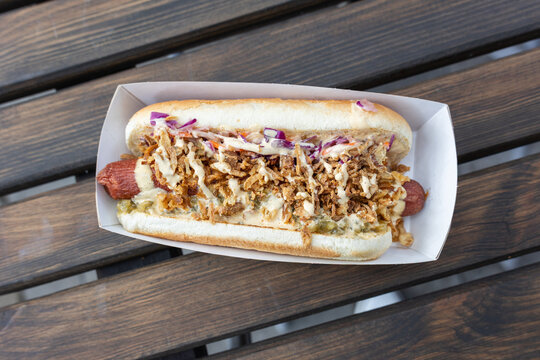 Top view of hot dog with crispy fried onions, cabbage and creamy sauce on wooden table