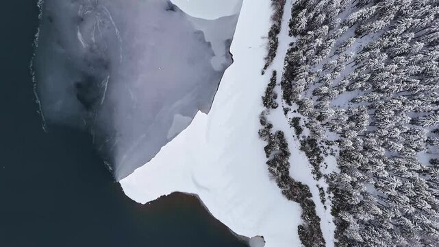 Aerial view of frozen Soboth Reservoir surrounded by snow-covered pine forests in the Weststeiermark region, Soboth Reservoir, Styria, Austria.
