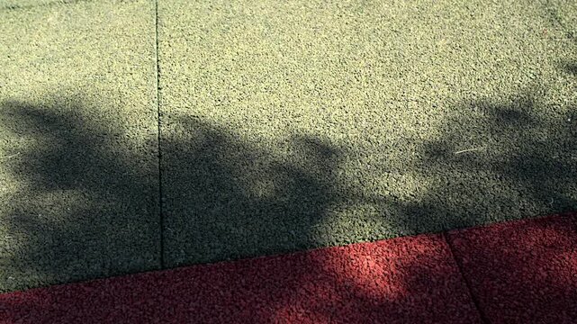 Dynamic plant silhouettes project over outdoor sports flooring while sunlight illuminates textured tiles. Swaying tree foliage creates relaxing ambient pattern across rubber safety pavement.