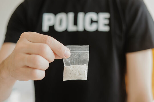 Police officer holding a plastic bag of white powder evidence. Concept of drug bust, narcotics investigation, law enforcement, and fighting crime.