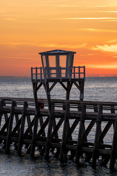 Luc-Sur-Mer, France - 08 08 2026:  Panoramic view of a wooden pier in front of the beach, sea, a colorful sunrise and Le Havre city far away