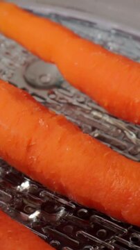 Macro shot of vibrant orange whole carrots placed on a metal steamer or grater plate during food preparation and cooking.