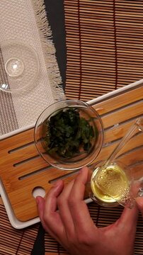 Top view of traditional Chinese tea ceremony setup on wooden tray. Wet tea leaves in glass gaiwan bowl, glass cup, and bamboo mat for authentic oriental tea drinking culture.