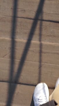 First person point of view perspective of someone walking in casual white sneakers along an outdoor wooden bridge or tiled walkway.