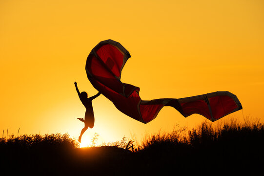 Silhouette of person jumping with a kite against sunset sky