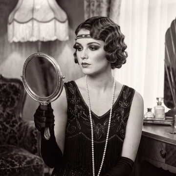 Vintage portrait of 1920s flapper woman looking into handheld mirror