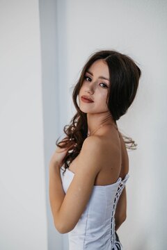 An elegant young woman in a white lace-up dress, looking over her shoulder; a portrait showing her bare back.