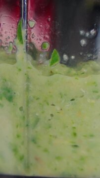 Healthy vegetable puree churns inside electric blender container during preparation. Appliance blends fresh green ingredients into thick beverage with energetic motion and precision.